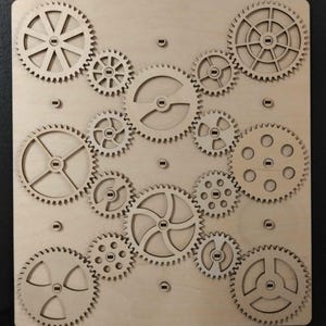 以下が含まれることがあります： さまざまなサイズの連動する歯車のコレクションを特徴とする木製パズル。歯車は明るい色の木材から切り出され、正方形の木製のベースに配置されています。機械的なテーマのデザイン。