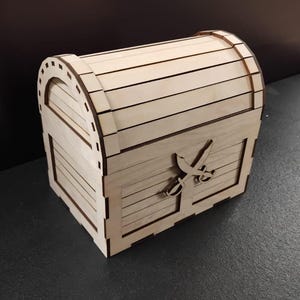 May include: A light-coloured wooden chest with a curved top and a rectangular base. The chest features a decorative design of crossed swords on the front. The chest is made of thin wooden slats and has a rustic, handcrafted appearance.