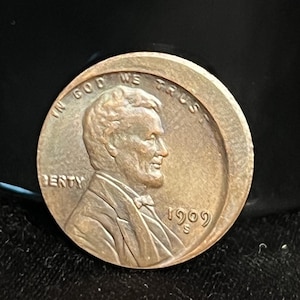 Puede incluir: Una moneda de cobre Lincoln de 1909. El anverso presenta un perfil de Abraham Lincoln, el texto "LIBERTY" y la fecha. La moneda también tiene el texto "IN GOD WE TRUST".