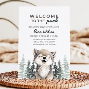 May include: A baby shower invitation with the text "WELCOME TO THE pack" at the top. The invitation features a watercolor illustration of a smiling wolf and evergreen trees. The invitation includes the name Sara Wilson, date, time, and location.