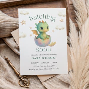 Puede incluir: Una invitación para un baby shower con una ilustración en acuarela de un bebé dragón saliendo de un huevo. El texto dice "hatching soon" e incluye los detalles del evento: fecha, hora y lugar. La invitación está en una tarjeta blanca.