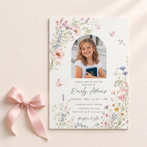 May include: A baptism invitation card featuring a central arched photo of a girl holding a book, surrounded by watercolor illustrations of wildflowers and butterflies. The text includes the name Emily Adams and event details in black font.