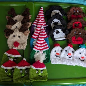 May include: A selection of handmade knitted hats in festive designs. Includes reindeer, Christmas trees, penguins, robins, snowmen, and Grinch-inspired hats. The hats are displayed on a green tray, ideal for the holiday season.