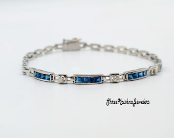 May include: A silver bracelet featuring rectangular blue gemstones and small clear stones. The bracelet has a delicate chain design and a clasp. The text "Shree Krishna Jewelers" is written in cursive.