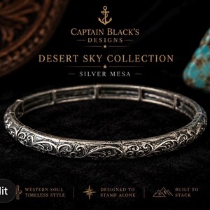 May include: Silver bracelet from the Desert Sky Collection. The bracelet features an ornate, engraved design. The image includes the text "Captain Black's Designs" and "Silver Mesa". The bracelet is designed to stand alone.