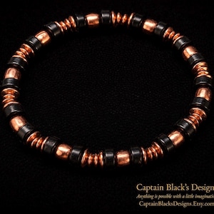 May include: A beaded bracelet featuring alternating black and copper-colored beads. The bracelet is made of small, round beads strung together, creating a flexible and stylish accessory. The bracelet is displayed on a black background.