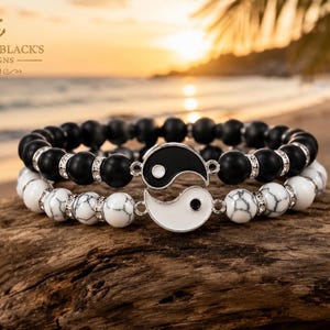 Puede incluir: Dos pulseras de cuentas con un dije de yin-yang. Una pulsera tiene cuentas negras mate, la otra tiene cuentas blancas veteadas. Ambas incluyen espaciadores plateados con pequeños cristales transparentes. El texto Captain Black's Designs es visible.