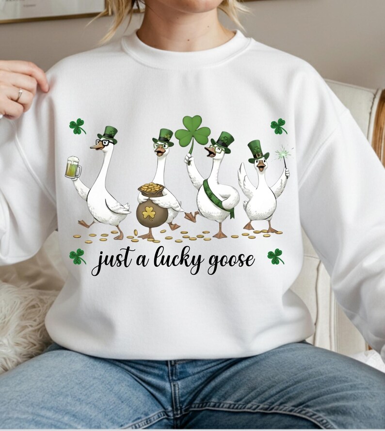 Puede incluir: Sudadera blanca con un dise&ntilde;o del D&iacute;a de San Patricio. El gr&aacute;fico muestra cuatro gansos de dibujos animados con sombreros verdes de copa y sosteniendo una cerveza, una olla de oro, un tr&eacute;bol y una bengala. El texto "just a lucky goose" est&aacute; debajo.
