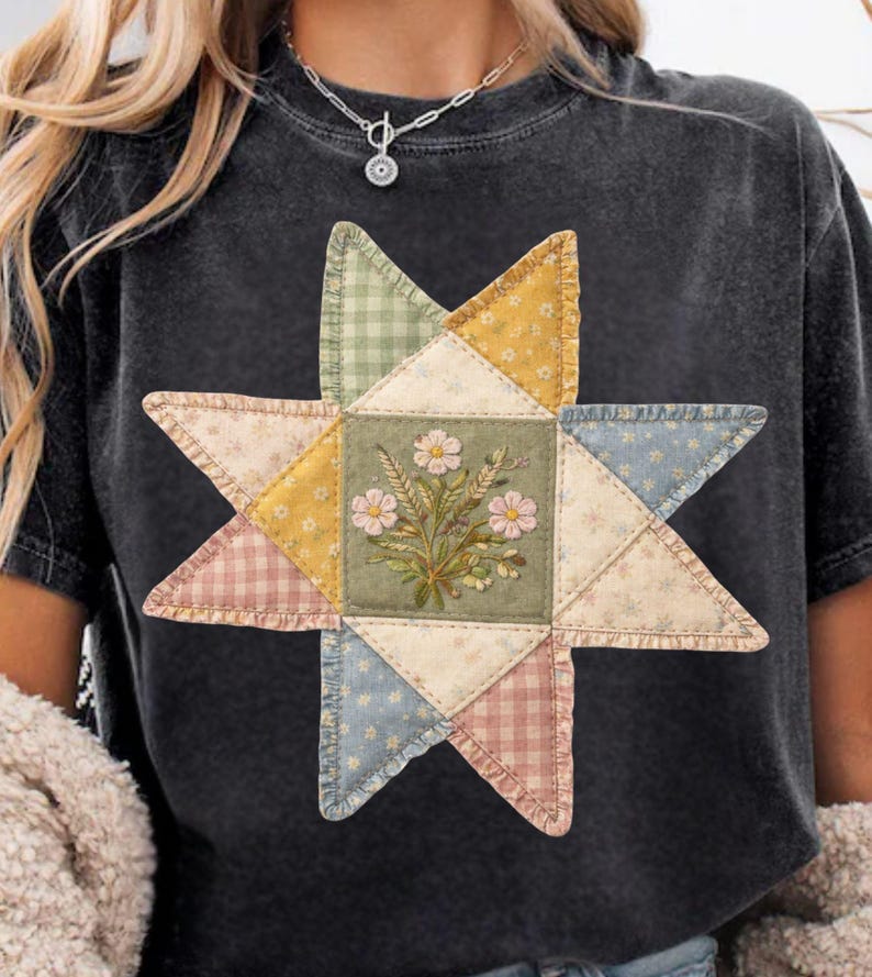 May include: Dark gray t-shirt featuring a star-shaped patchwork design. The star is composed of various fabric patterns, including gingham and floral prints, with a central square showcasing a floral bouquet. The design incorporates pastel colors.