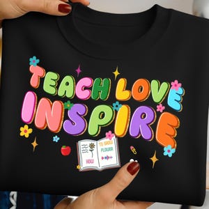 May include: Black sweatshirt with the words "TEACH LOVE INSPIRE" in colorful bubble letters. The design includes flowers, stars, and an open book with the text "TO GROW FLOWER".