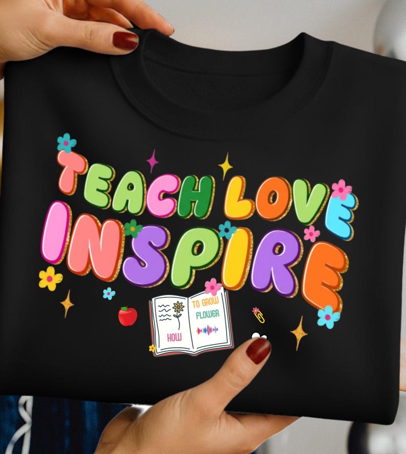 May include: Black sweatshirt with the words "TEACH LOVE INSPIRE" in colorful bubble letters. The design includes flowers, stars, and an open book with the text "TO GROW FLOWER".