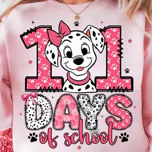 Könnte beinhalten: Hellrosa Sweatshirt mit einem Aufdruck eines Dalmatiner-Hundes mit rosa Schleife und Halsband. Die Zahl "111" wird mit rosa Pfotenabdrücken angezeigt, und der Text "DAYS of school" steht darunter. Das Design umfasst Pfotenabdrücke und Sterne.