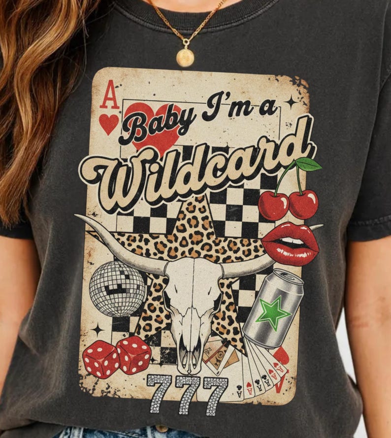May include: Dark gray t-shirt featuring a graphic with a playing card design. The design includes a bull skull, cherries, dice, and the text "Baby I'm a Wildcard" and "777". The shirt has a vintage, distressed look.