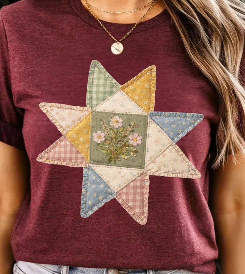 May include: Burgundy t-shirt featuring a patchwork star design. The star is composed of various patterned fabrics in pastel colors, with a central square showcasing embroidered flowers. The overall design has a vintage, handcrafted aesthetic.