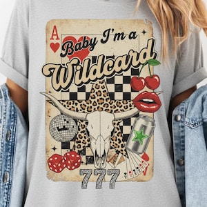 May include: A gray t-shirt featuring a vintage-style graphic with the text "Baby I'm a Wildcard." The design includes a playing card, cherries, dice, a disco ball, a bull skull, and a can.