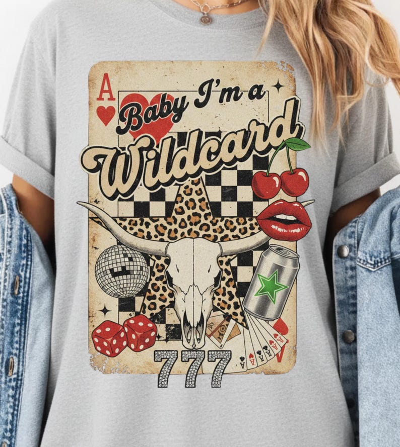 May include: A gray t-shirt featuring a vintage-style graphic with the text "Baby I'm a Wildcard." The design includes a playing card, cherries, dice, a disco ball, a bull skull, and a can.