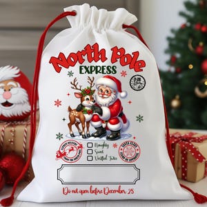 May include: White drawstring Christmas gift bag with red accents. The bag features a graphic of Santa Claus and a reindeer, with text that reads "North Pole Express." Additional text includes "Do not open before December 25."