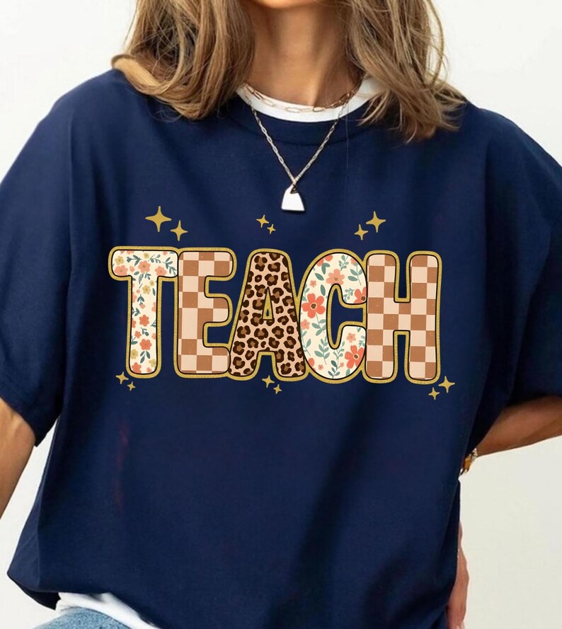 May include: Navy blue sweatshirt with the word "TEACH" in a decorative font. The letters are adorned with floral, leopard print, and checkered patterns, with gold star accents.
