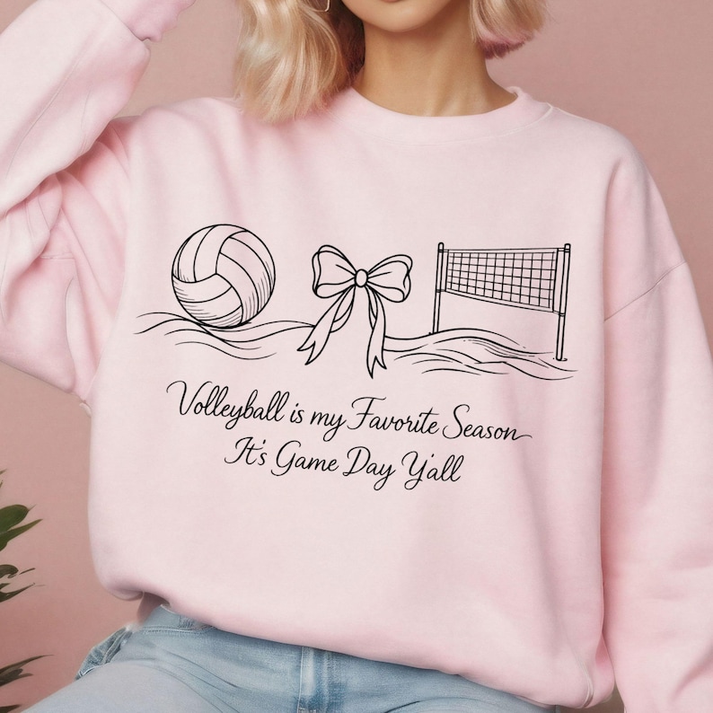 May include: A light pink sweatshirt with a black graphic of a volleyball, a bow, and a volleyball net. The text "Volleyball is my Favorite Season It's Game Day Y'all" is printed below the graphic.