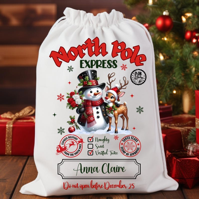 May include: White drawstring gift bag with a festive design. The bag features the text "North Pole Express" in red, along with illustrations of a snowman and a reindeer. Includes the name "Anna Claire" and the message "Do not open before December 25".
