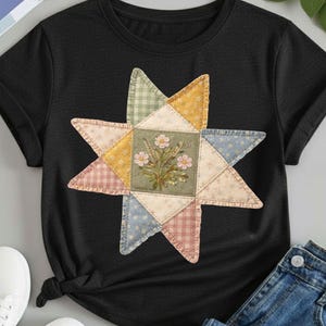 May include: Black t-shirt featuring a colorful star-shaped design. The star is composed of patchwork squares in various pastel colors, with a central square showcasing a floral bouquet. The shirt is made of a soft material.