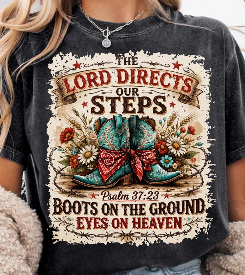 May include: Black t-shirt featuring a graphic with turquoise cowboy boots, a red bandana, and floral accents. The text reads "The Lord Directs Our Steps" and "Boots on the Ground, Eyes on Heaven."