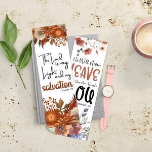 May include: Two white bookmarks with floral designs and inspirational quotes. One bookmark reads "The Lord is my light and my salvation." The other says "He will never leave you." A pink watch and a cup are also in the image.