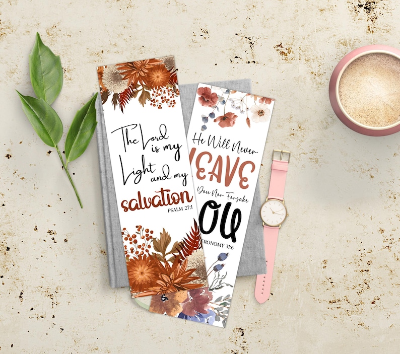 May include: Two white bookmarks with floral designs and inspirational quotes. One bookmark reads "The Lord is my light and my salvation." The other says "He will never leave you." A pink watch and a cup are also in the image.