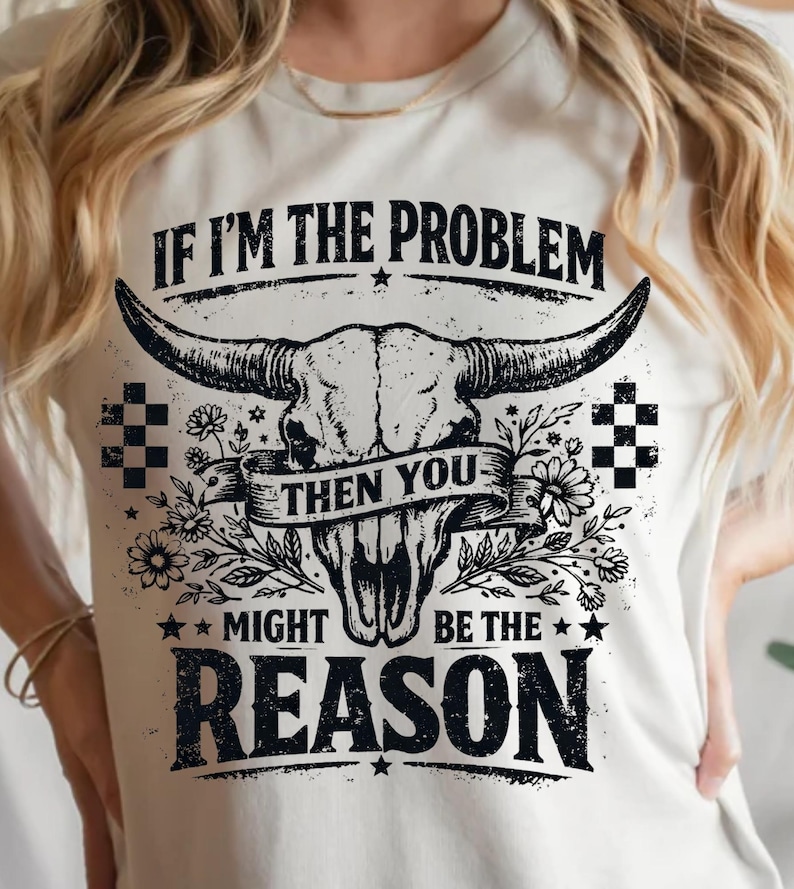 May include: Cream-colored t-shirt featuring a black and white graphic of a bull skull with large horns, floral accents, and the text "IF I'M THE PROBLEM THEN YOU MIGHT BE THE REASON."