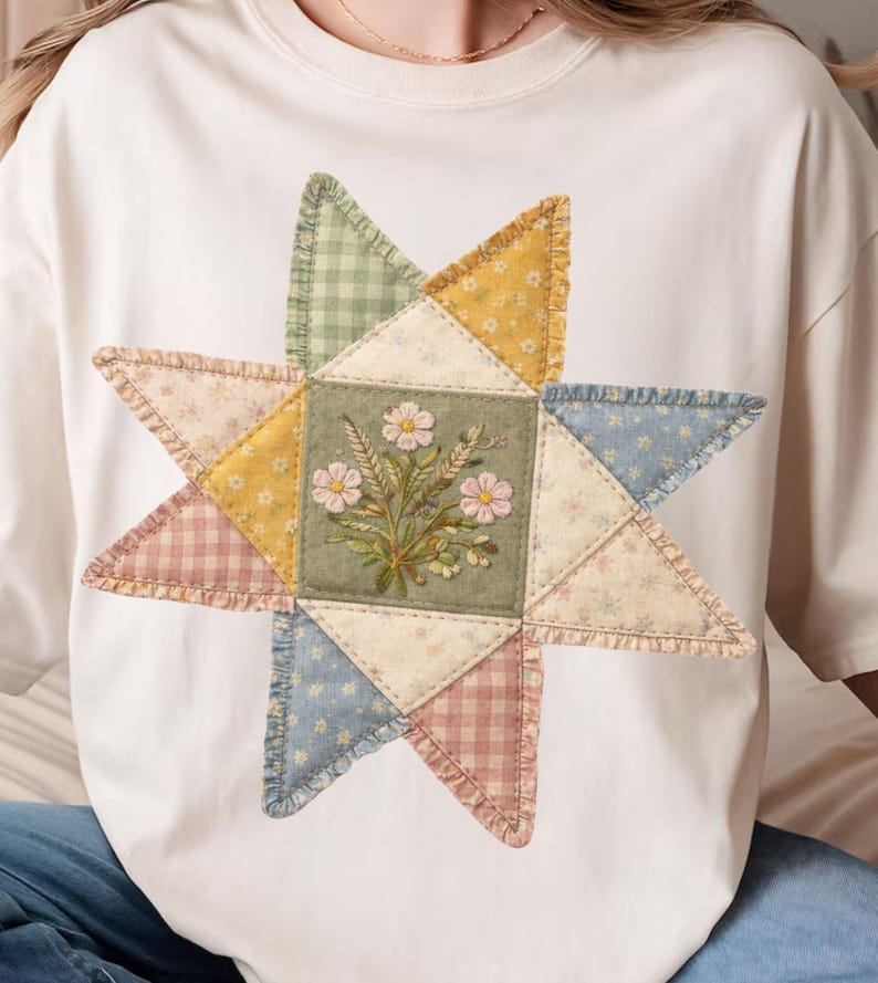 May include: Cream-colored t-shirt featuring a large, colorful star design. The star is composed of various fabric patches in pastel shades of pink, yellow, blue, and green, with a central square embroidered with flowers.
