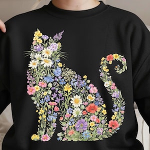 May include: Black sweatshirt featuring a floral cat design. The cat silhouette is filled with colorful flowers, including daisies, poppies, and lavender. The flowers are in shades of pink, yellow, blue, and purple.