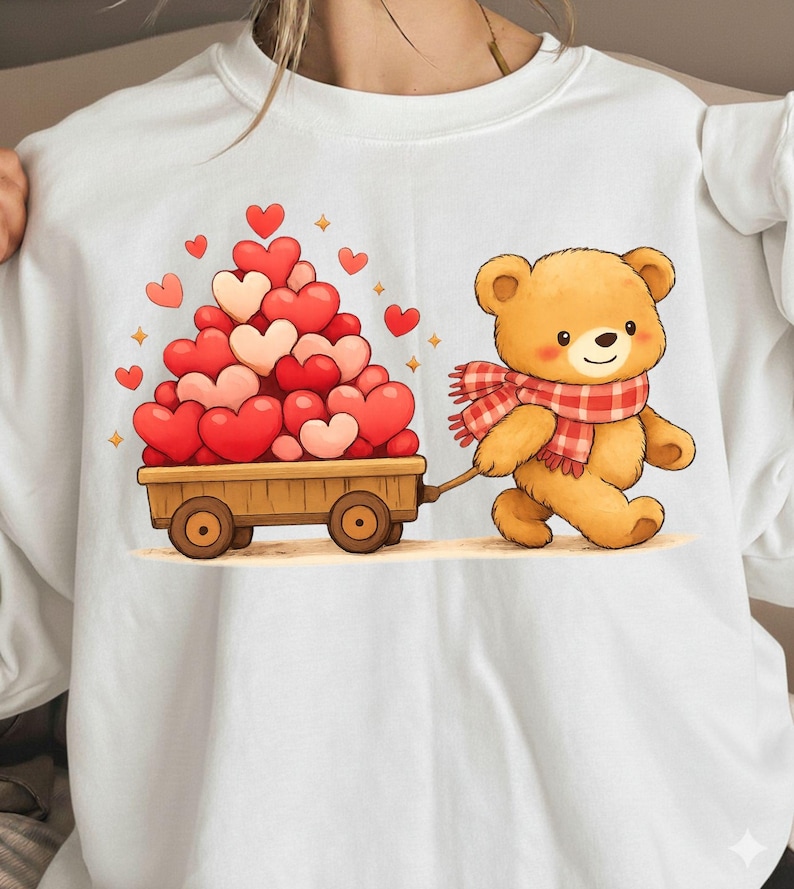 May include: White sweatshirt with a cartoon teddy bear pulling a wooden cart laden with red and pink hearts. The bear is wearing a red and white checked scarf. A cute design for Valentine's Day or a special gift.