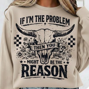 May include: Beige sweatshirt with a graphic of a bull skull, flowers, and the text "IF I'M THE PROBLEM THEN YOU MIGHT BE THE REASON". The design is in black and white, with a vintage, distressed look.