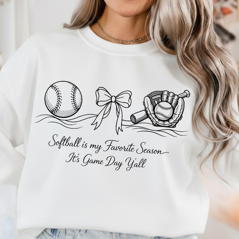 May include: White sweatshirt with a black graphic of a softball, bow, and glove with a softball inside. The text reads "Softball is my Favorite Season, It's Game Day Y'all."