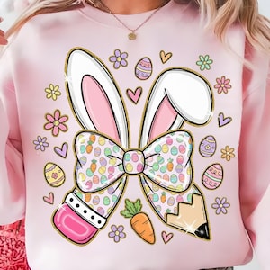 May include: A light pink sweatshirt featuring a whimsical Easter design. The design includes bunny ears, a bow tie, a pencil, Easter eggs, flowers, hearts, and a carrot. The bunny ears and pencil are outlined in gold.