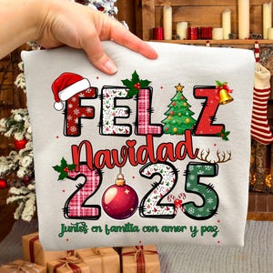 Peut inclure: Un coussin de Noël de couleur claire avec les mots "FELIZ Navidad 2025" en rouge, vert et blanc. Le motif comprend un bonnet de Père Noël, un sapin de Noël, des ornements et la phrase "juntos en familia con amor y paz".