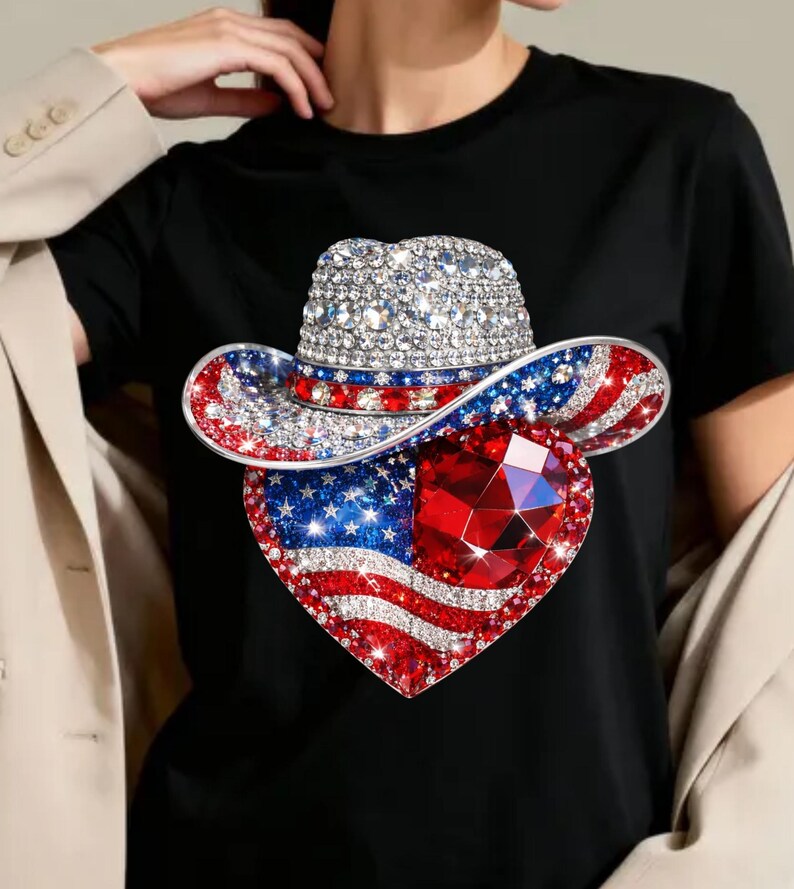 May include: Black t-shirt featuring a rhinestone-studded cowboy hat and a heart-shaped American flag design. The hat has a silver crown, red and blue brim, and the heart has a large red gem.