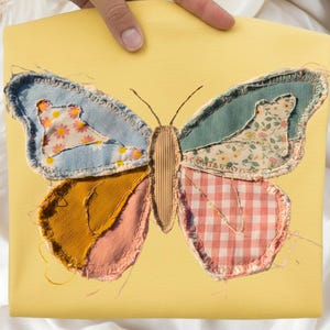 Peut inclure: Un tissu jaune avec une grande application de papillon. Les ailes du papillon sont en patchwork, avec des sections de denim, de motifs floraux et de vichy. Le corps du papillon est en matériau texturé de couleur beige.