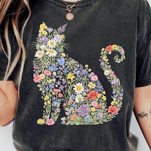 May include: Dark gray t-shirt featuring a floral cat design. The cat silhouette is filled with colorful flowers in shades of yellow, pink, purple, and blue. The shirt has a vintage, washed look.