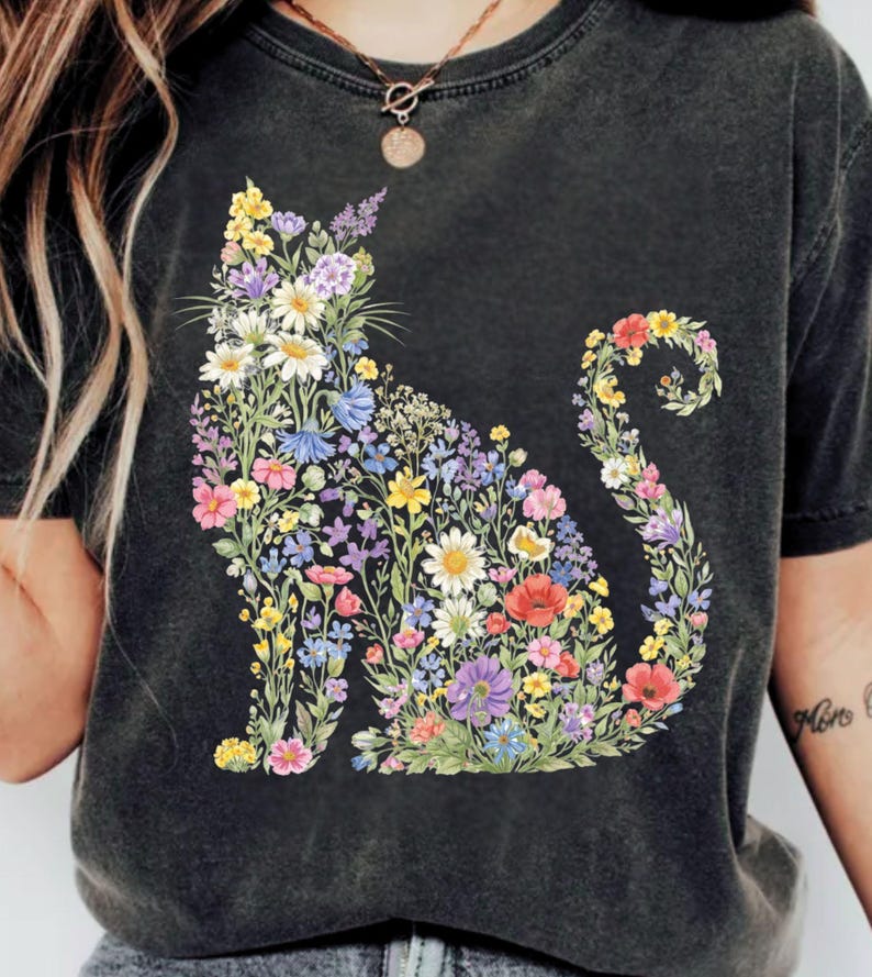 May include: Dark gray t-shirt featuring a floral cat design. The cat silhouette is filled with colorful flowers in shades of yellow, pink, purple, and blue. The shirt has a vintage, washed look.
