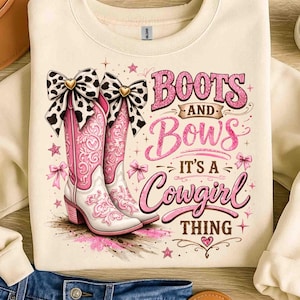 Op de afbeelding: Crèmekleurige sweatshirt met een afbeelding van roze cowboylaarzen en strikken, en de tekst "Boots and Bows It's a Cowgirl Thing." De laarzen hebben witte details en een bloemenpatroon. De strikken zijn zwart en wit.