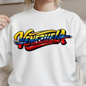 Puede incluir: Sudadera blanca con la palabra "VENEZUELA" en un diseño vibrante y estilizado. La tipografía incorpora los colores de la bandera venezolana: amarillo, azul y rojo, con detalles de estrellas.