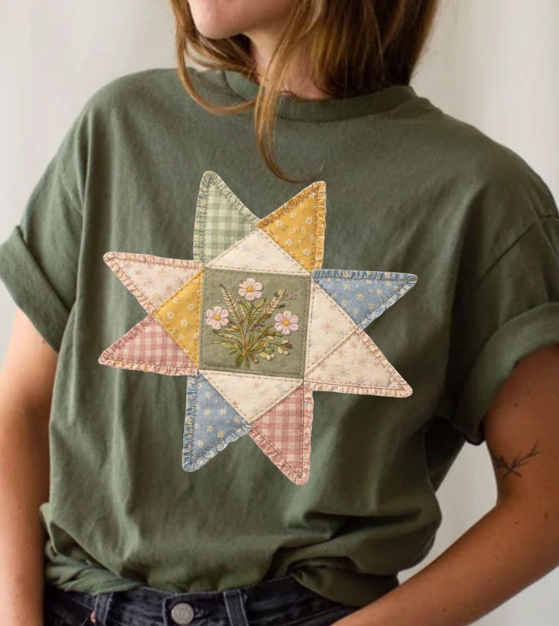 May include: An olive green t-shirt featuring a patchwork star design. The star is composed of various fabric patterns and colors, including floral embroidery, gingham, and pastel hues. The shirt has short sleeves and a relaxed fit.
