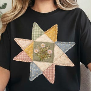 May include: Black t-shirt featuring a colorful starburst design. The starburst is made of patchwork fabric in various pastel colors, with a floral centerpiece. The design has a vintage, handcrafted aesthetic.