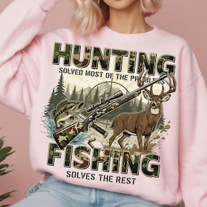 May include: Pink sweatshirt with a graphic featuring a rifle, deer, and fish, with the text "HUNTING SOLVED MOST OF THE PROBLEMS FISHING SOLVES THE REST". The design includes a forest and sun.