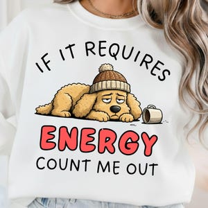 May include: White sweatshirt featuring a cartoon dog wearing a brown beanie and a coffee mug. The text reads "If it requires energy, count me out" in black and red.