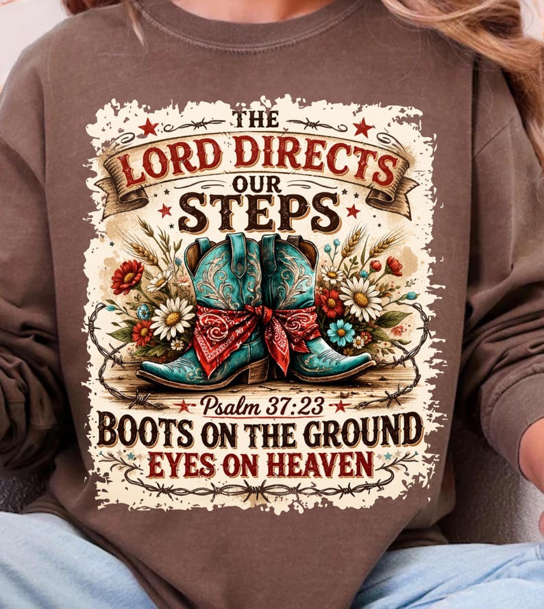 May include: Brown sweatshirt with a graphic design featuring turquoise cowboy boots, a red bandana, and floral accents. The text reads "The Lord Directs Our Steps" and "Boots on the Ground Eyes on Heaven."