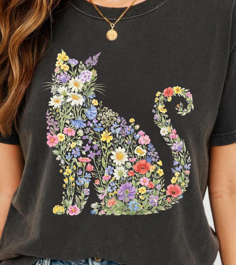 May include: Black t-shirt featuring a floral cat design. The cat silhouette is filled with colorful flowers, including daisies, poppies, and lavender. The shirt has a crew neck and short sleeves, and is made of a soft, dark fabric.