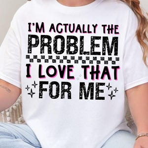May include: White t-shirt with the text "I'M ACTUALLY THE PROBLEM I LOVE THAT FOR ME" in black and pink lettering. The shirt has a checkered pattern and star accents.