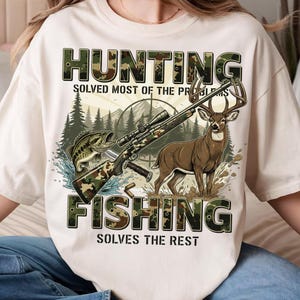May include: Cream-colored t-shirt with a graphic featuring a deer, a rifle, and a fish. The text reads "HUNTING SOLVED MOST OF THE PROBLEMS, FISHING SOLVES THE REST." The design incorporates camouflage patterns and outdoor elements.